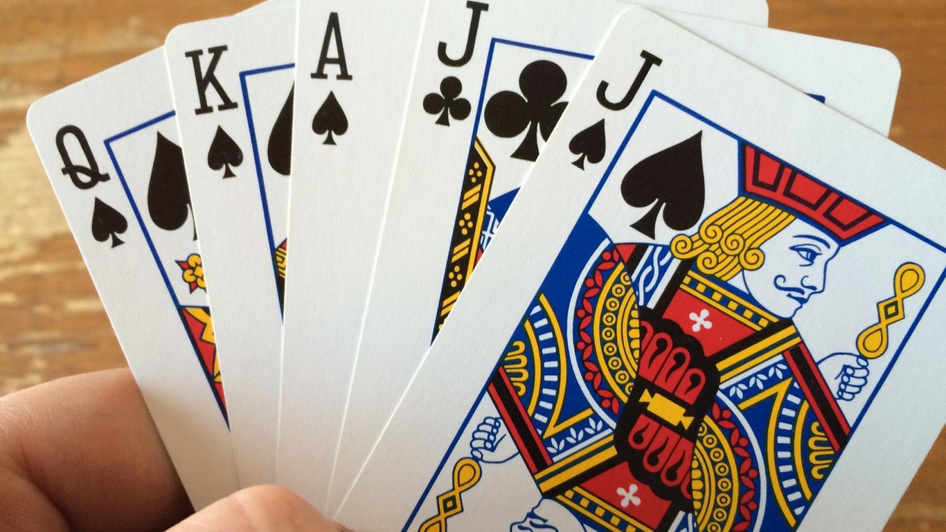 A hand holding a royal flush in spades and clubs.