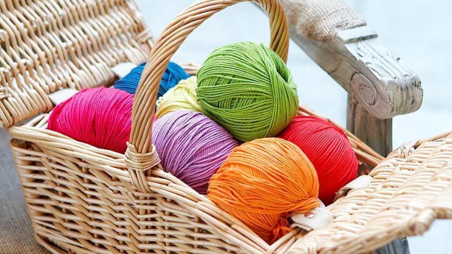 Colorful yarn balls in a wicker basket on a chair.